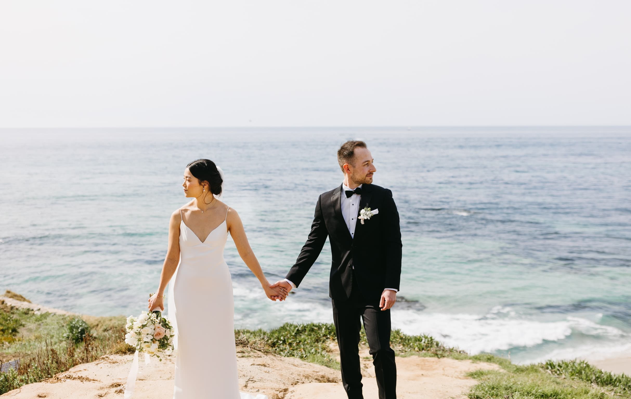 James and his wife holding hands in wedding attire above the Pacific Ocean